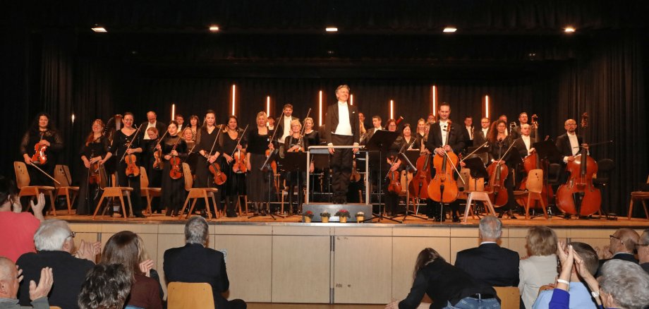 Mehrere in schwarz gekleidete Personen sitzend mit Musikinstrumenten auf einer Bühne