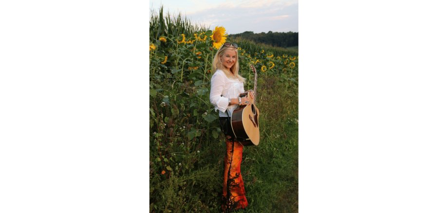 Blonde Frau mit Gitarre, stehend im Sonnenblumenfeld