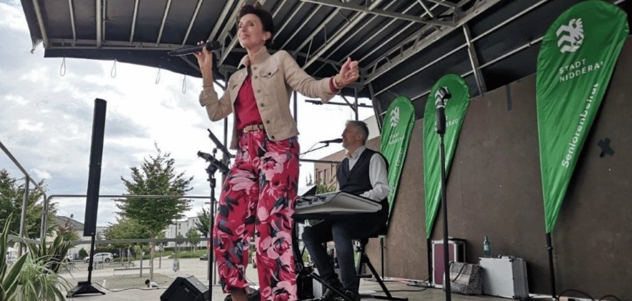 Frau singend und bunt gekleidet mit Mikrofon auf einer mobilen Bühne im Freien