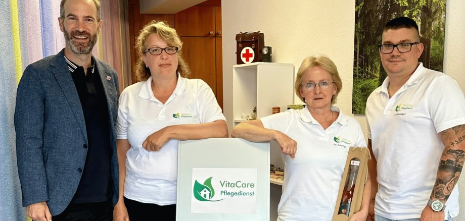 Zwei Männer und zwei Frauen stehend vor einem Plakat mit der Aufschrift Vita Care Pflegedienst