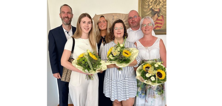 4 Frauen und 2 Männer stehend mit Blumen in der Hand