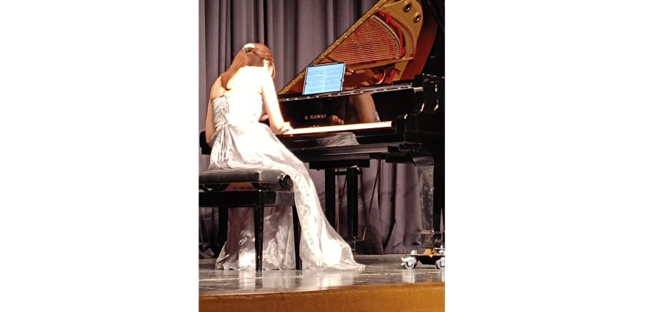 Dame mit schwarzen langen Haaren sitzend in einem hellen Kleid am Klavier