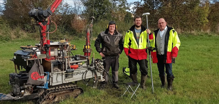 Drei Männer stehend mit einem Arbeitsgerät auf einer Wiese