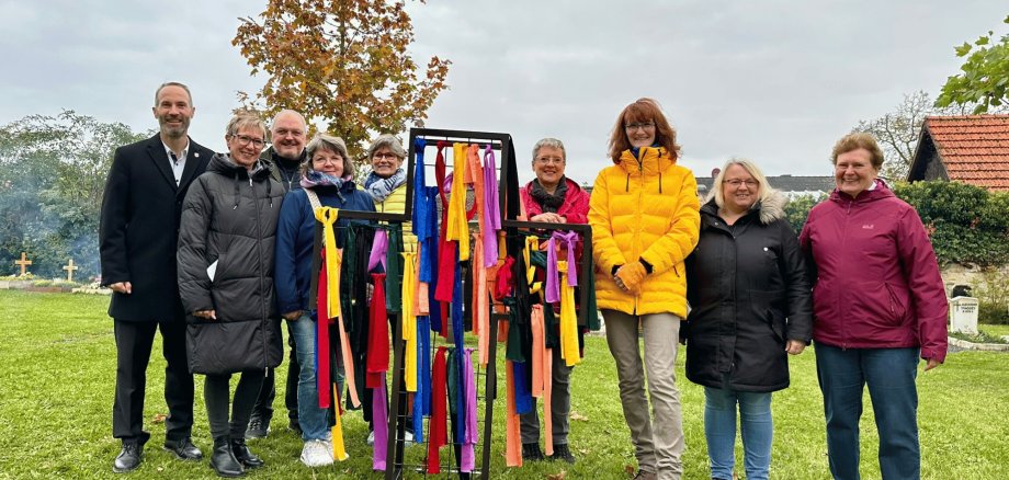 Mehrere Personen stehend auf einem Friedhof mit mehreren bunten Bändern