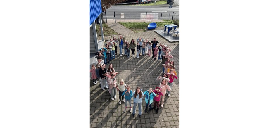 Kinder stellen sich auf einem Hof zu einem großen Herz zusammen