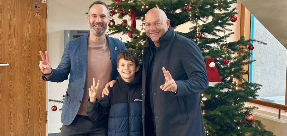 Zwei Männer und ein Junge vor einem dekorierten Weihnachtsbaum im Foyer des Rathauses