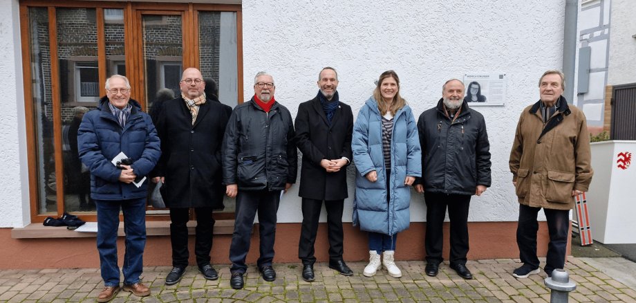 Sechs Männer und eine Frau stehend vor der Hausfassade eines weißen Hauses mit dunklem Schriftzug "Monica Kingreen Haus"